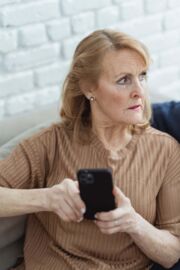 Eine Seniorin hält ein Smartphone in der Hand und ist besorgt.