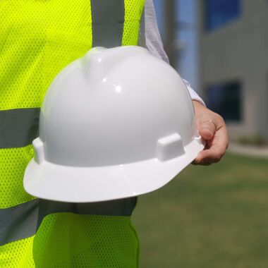 Ein Arbeiter mit Warnweste hält einen weißen Schutzhelm vor sich in der Hand.