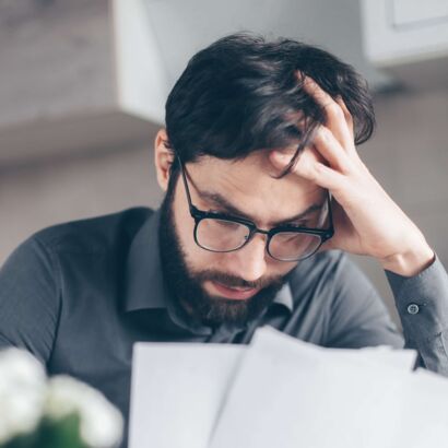Ein jüngerer Mann mit Brille liest konzentriert und bedenklich ein Dokument